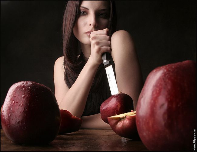 A woman with a knife and a cut apple, with red delicious apples in the foreground