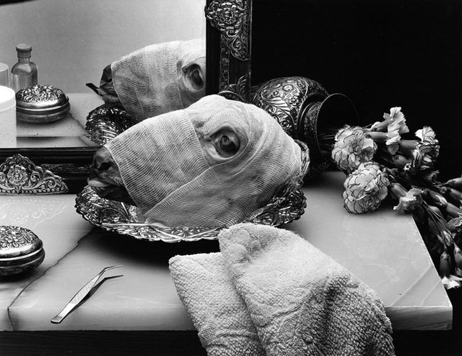 Black and white photo of a goat's head wraped in bandages sitting in an ornate tray.
